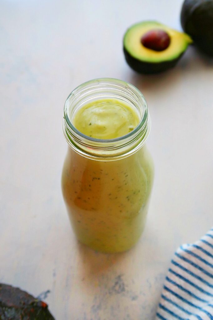 Avocado salad dressing in a tall glass on a board.